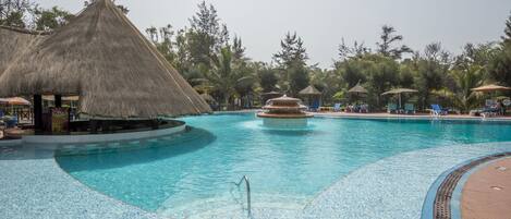 A swimming pool with a thatched-roof structure, lounge chairs, and palm trees.