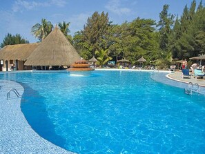 Una piscina grande con una estructura de techo de paja y sillas de descanso.