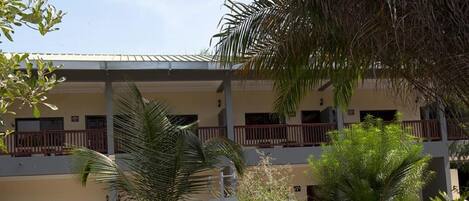 A two-story building with a flat roof, balconies, and a well-maintained garden with palm trees and shrubs.
