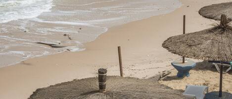 Una playa con sombrillas de paja y una orilla arenosa.