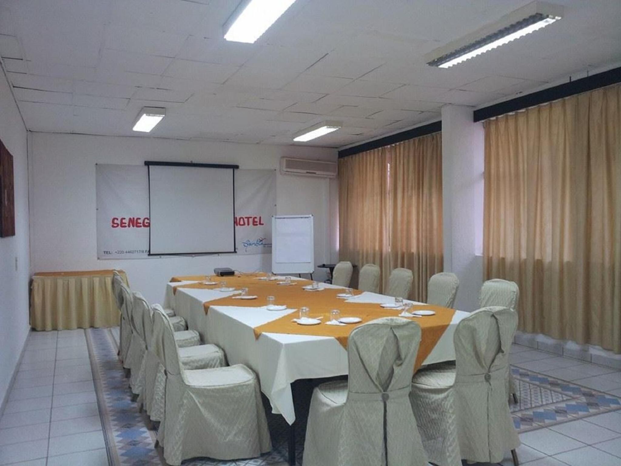 A conference room with a long table, chairs, a projector screen, and curtains.