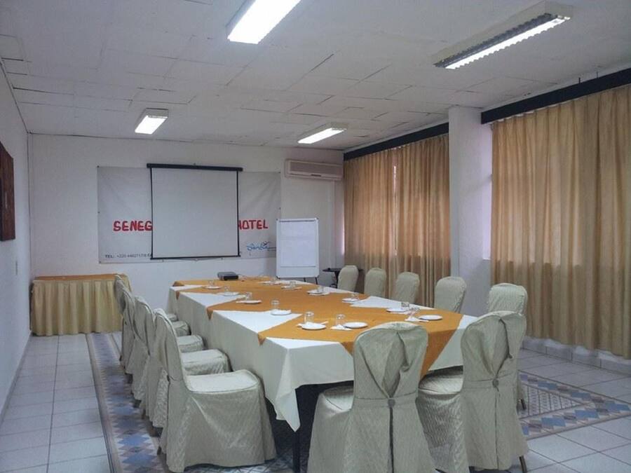 Un salón de conferencias con una larga mesa, sillas, una pantalla de proyector y cortinas.