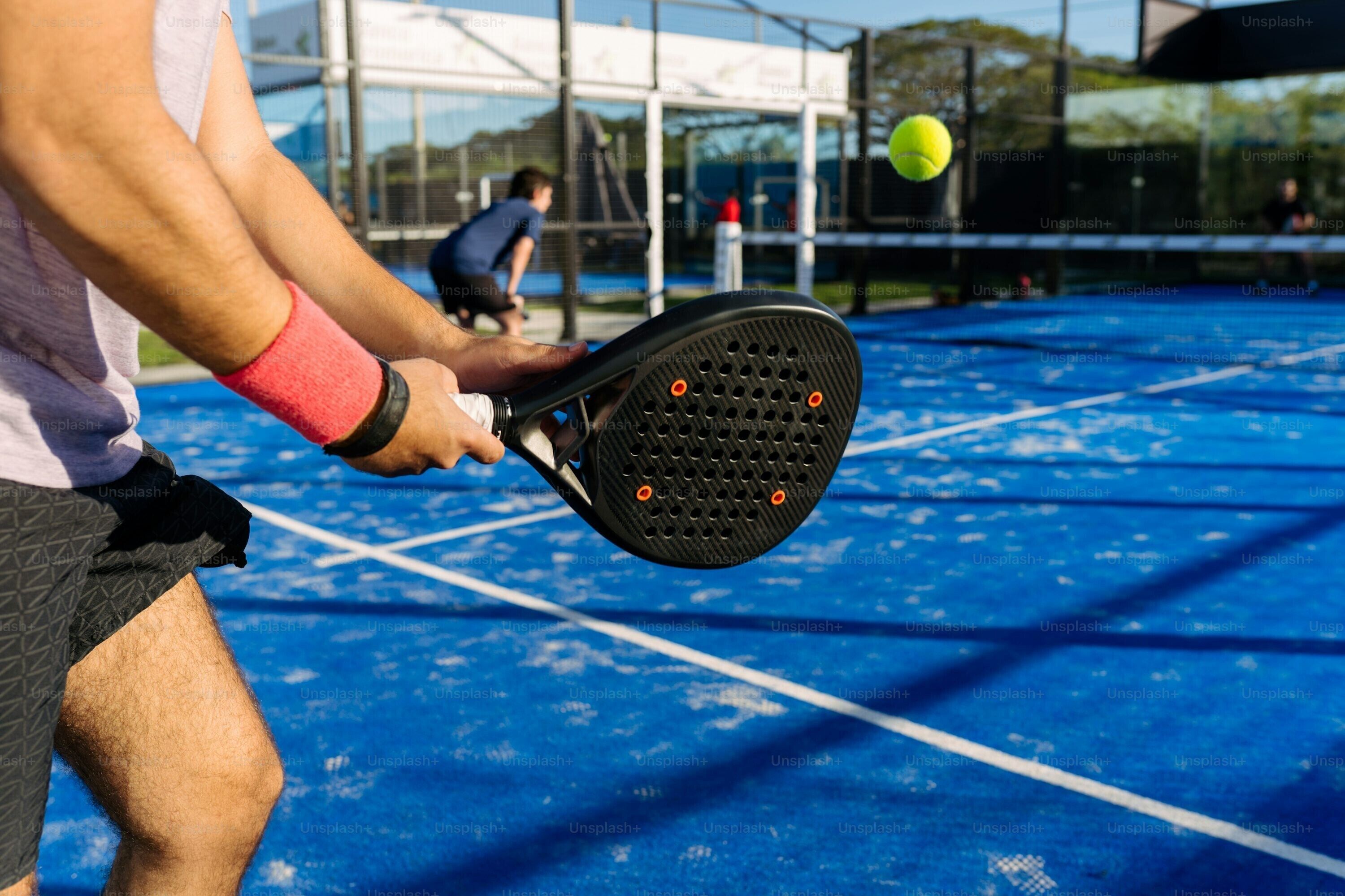 Un court de tennis avec un joueur tenant une raquette, une balle de tennis en l’air et une bouteille d’eau par terre.