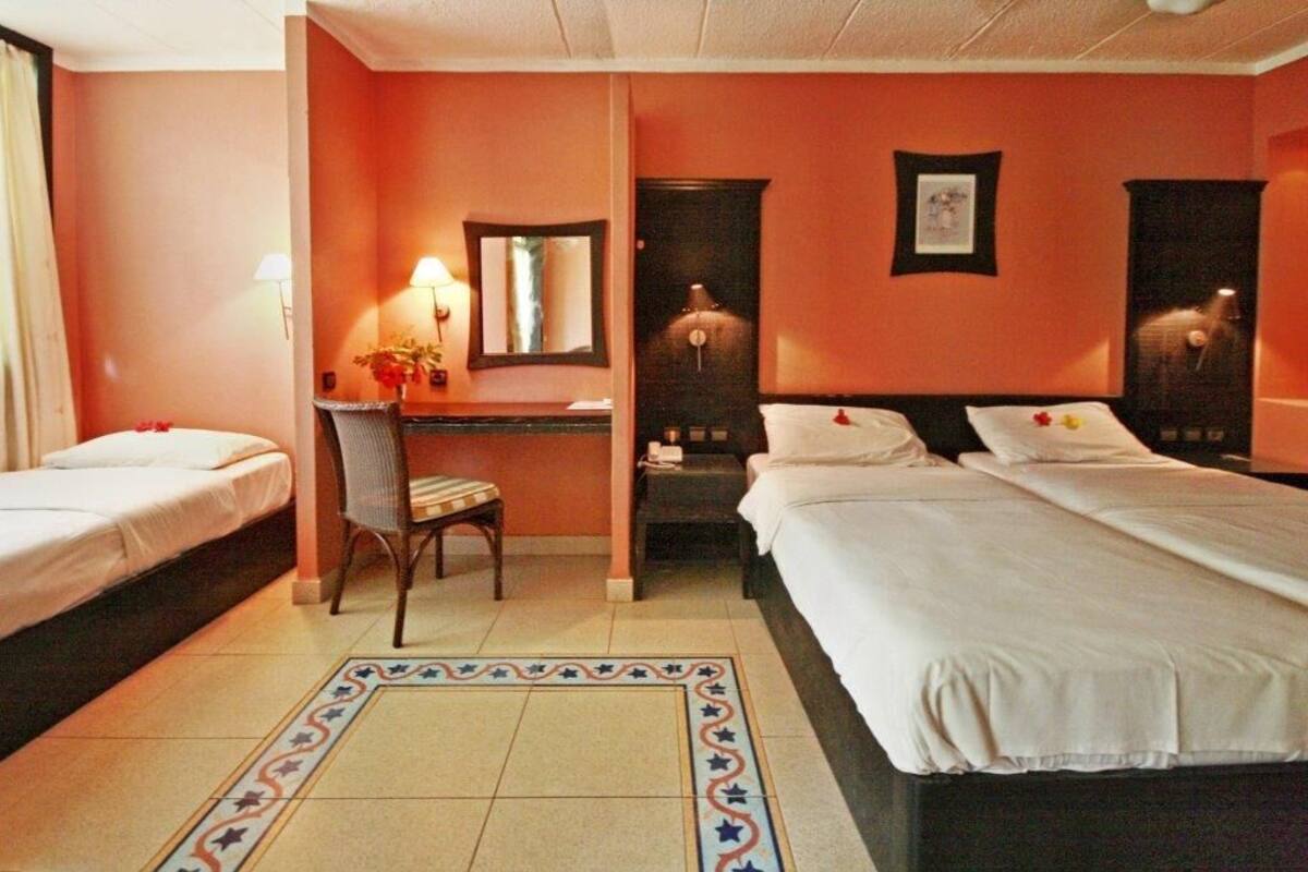 Ein Hotelzimmer mit zwei Betten, einem Schreibtisch, einem Sessel und einem kleinen Tisch mit einer Lampe.