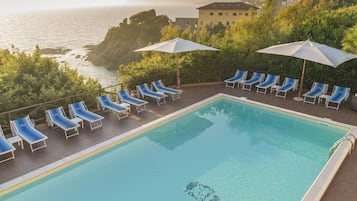 Una piscina con sillones de playa y sombrillas, con vistas a una zona costera con edificios y vegetación.