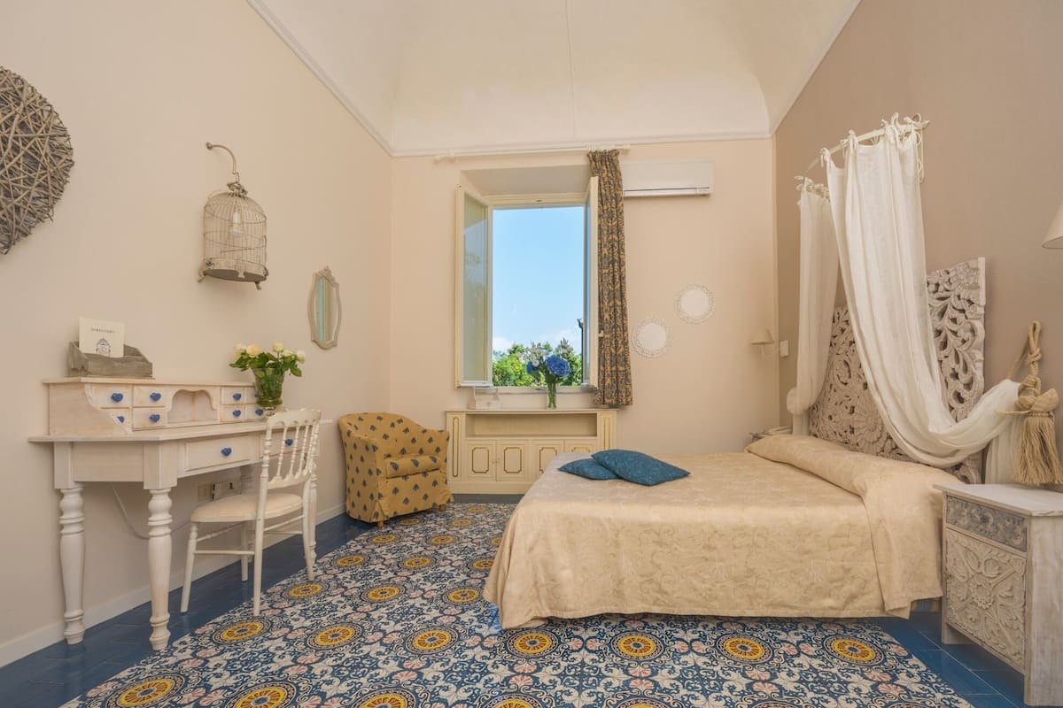 A bedroom with a bed, a desk, a chair, a mirror, and a window with curtains.