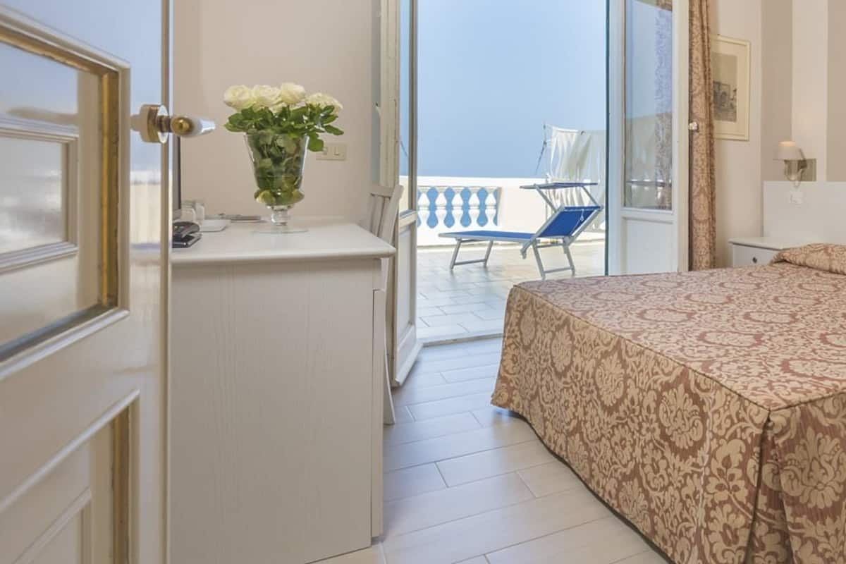 A bedroom with a bed, a small table with a vase of flowers, and a balcony with a chair.
