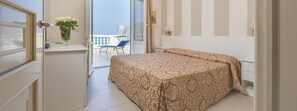 A bedroom with a bed, a small table with a vase of flowers, and a balcony with a chair. - Grand Hotel Villa Parisi (Rosignano Marittimo)