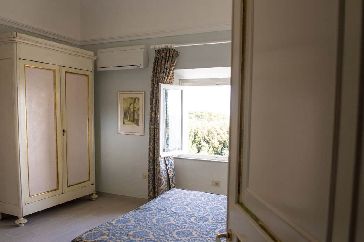A bedroom with a bed, a wardrobe, a window with curtains, and a wall-mounted air conditioner.