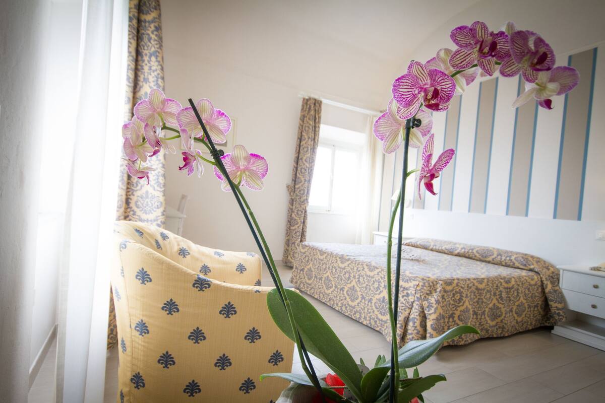 A bedroom with a bed, a chair, and a potted orchid plant.