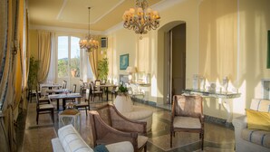 A spacious dining area with a high ceiling, chandeliers, and a view of the outdoors. - Grand Hotel Villa Parisi (Rosignano Marittimo)