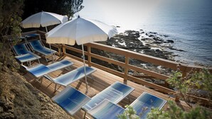 A wooden deck with sun loungers and white umbrellas overlooking a rocky coastline. - Grand Hotel Villa Parisi (Rosignano Marittimo)