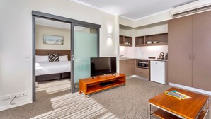 A hotel room with a bed, TV, wooden coffee table, kitchenette, and sliding doors. - New Haus Managed by Hougoumont (Fremantle)