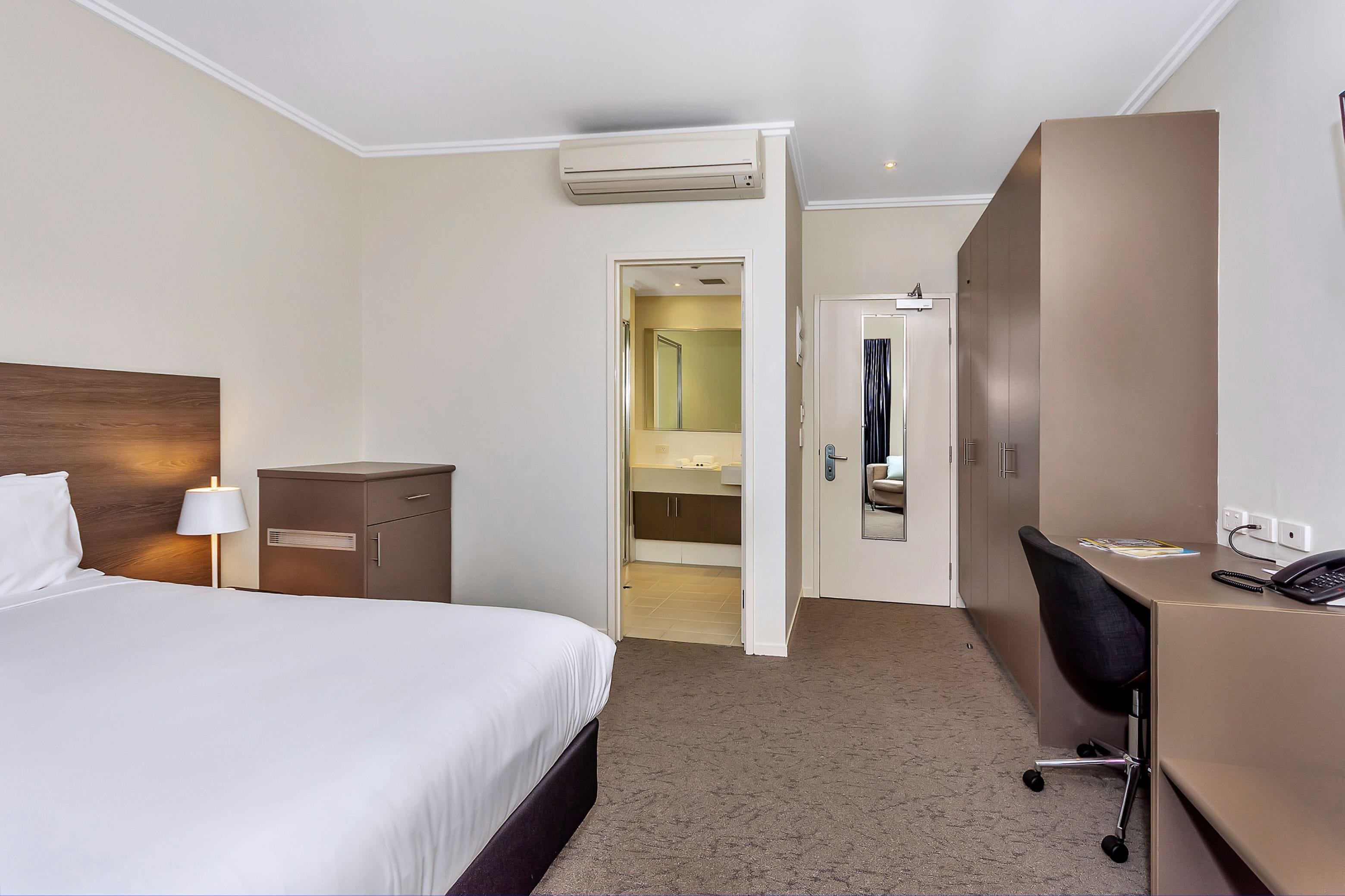 Habitación de hotel con cama, escritorio, armario y baño visible a través de una puerta abierta.