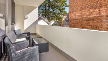 Ein Balkon mit Korbmöbeln und einem Glastisch, mit Blick auf ein Backsteinhaus und einen Baum.