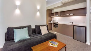 A compact living space with a sofa, a coffee table, a kitchenette, and a built-in oven. - New Haus Managed by Hougoumont (Fremantle)