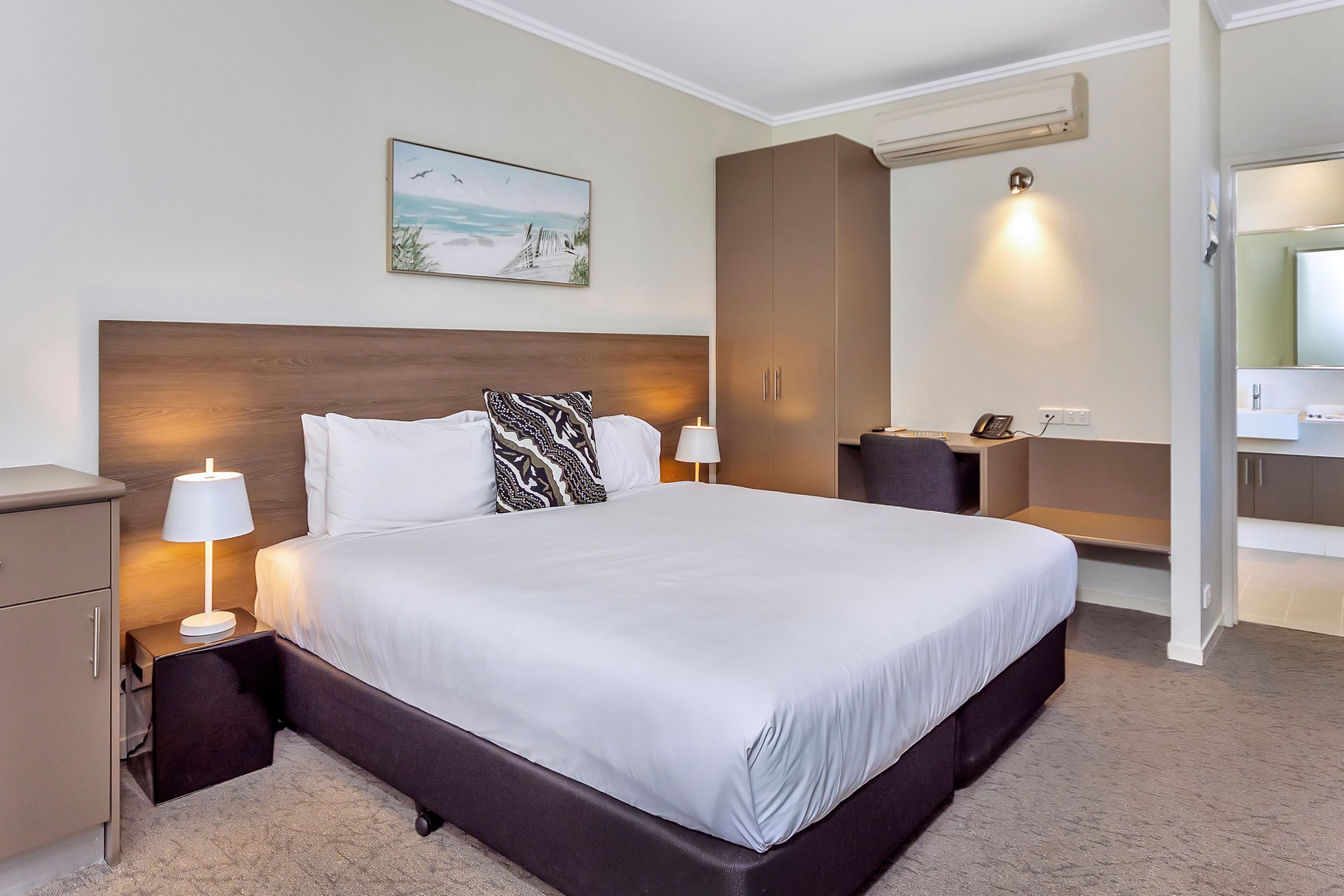A hotel room with a large bed, two bedside tables with lamps, a wardrobe, and a painting on the wall.
