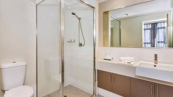 A modern bathroom with a glass-enclosed shower, a white toilet, and a vanity with a large mirror and a sink.