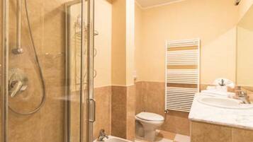 Een badkamer met een douchecabine van glas, een bidet en een wastafel met spiegel.