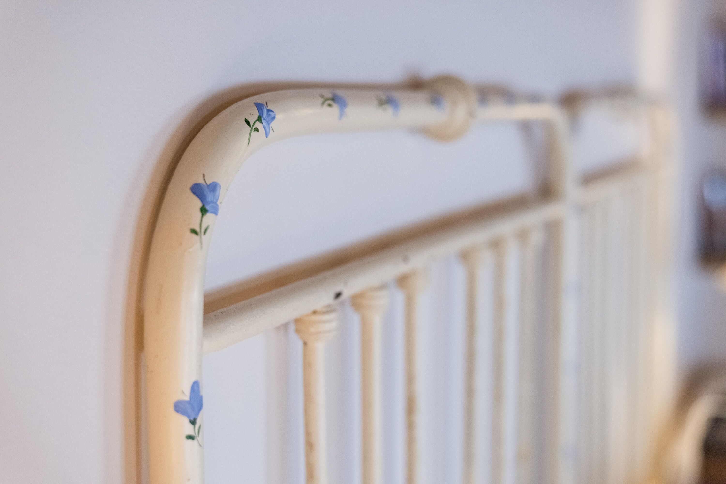 A close-up of a white metal bed frame with blue floral decorations.