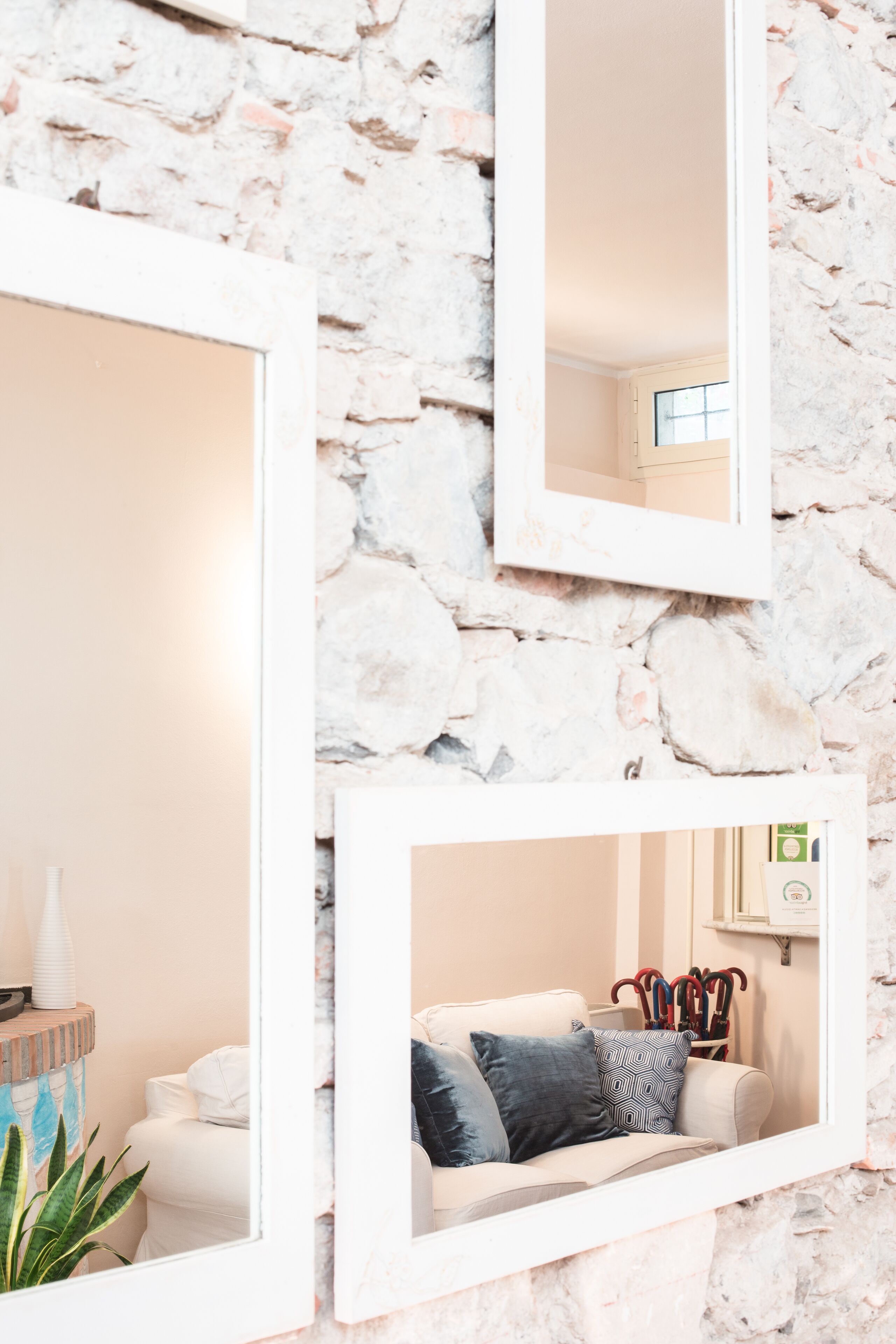 Una habitación con pared de piedra, un sofá blanco con cojines estampados y un espejo que refleja la estancia.