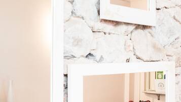 Una habitación con pared de piedra, un sofá blanco con cojines estampados y un espejo que refleja la estancia.