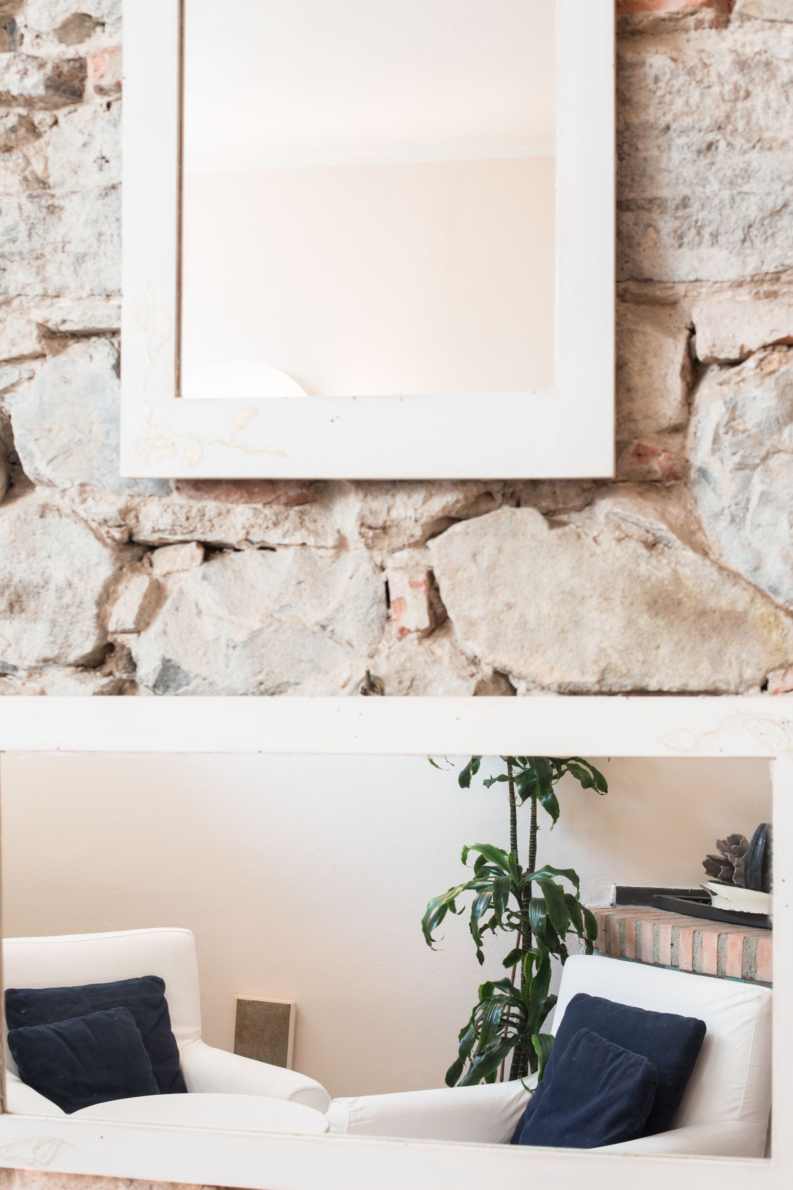 A living room with a white sofa, two dark cushions, a potted plant, and a stone wall.