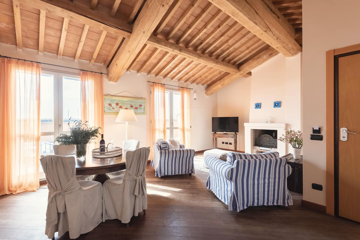 A cozy living room with wooden beams, a TV, a fireplace, and striped sofas.