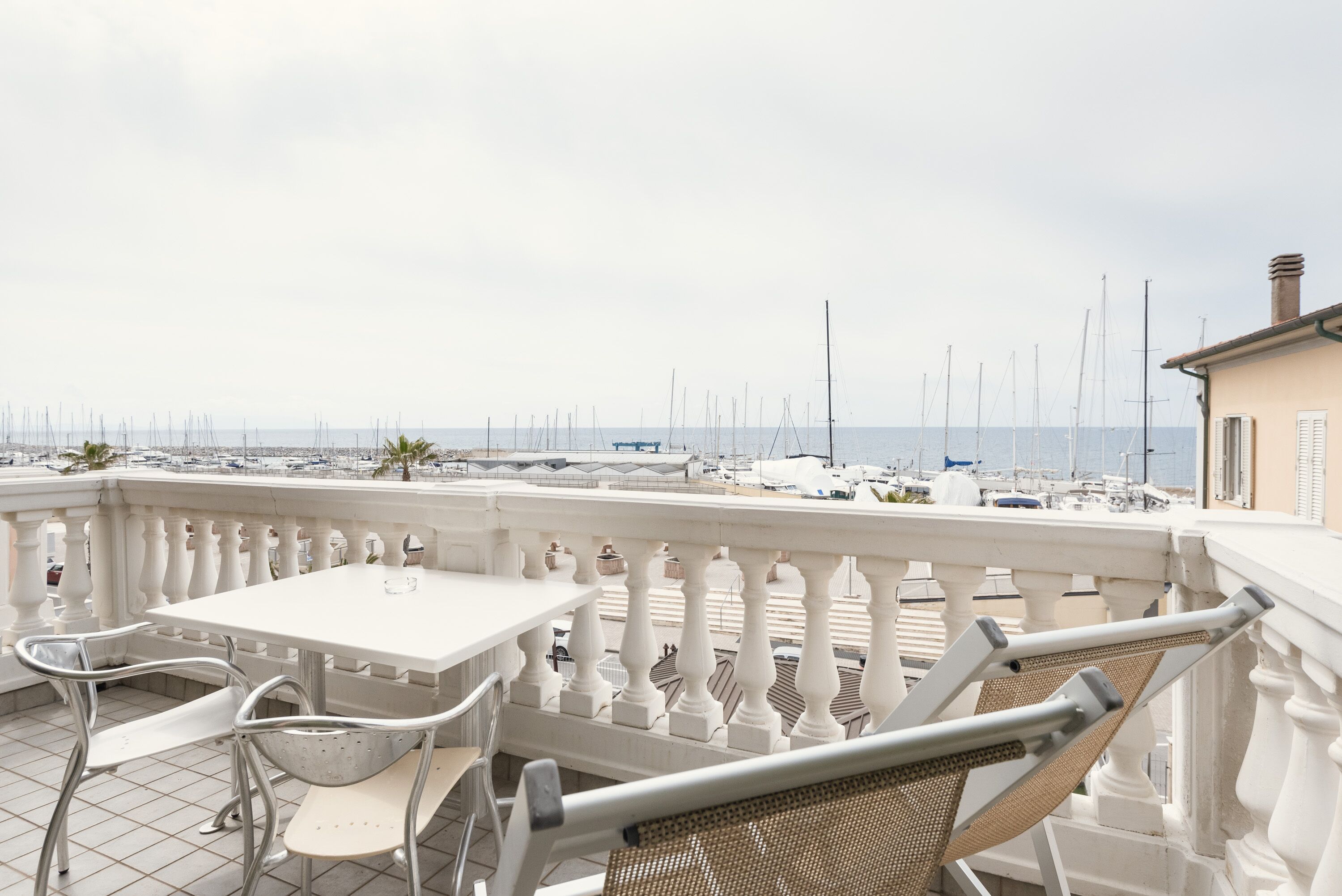 A balcony with a white table and chairs, overlooking a marina with boats and yachts.