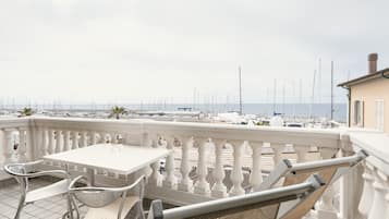 A balcony with a white table and chairs, overlooking a marina with boats and yachts.