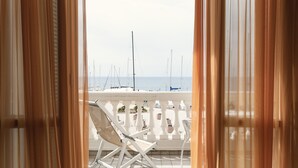 Een balkon met een witte stoel en tafel, met uitzicht op een jachthaven met zeilboten.