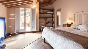 Een slaapkamer met een houten plafond, een bed met een witte dekbedovertrek, een kledingkast en een klein tafeltje met een lamp.