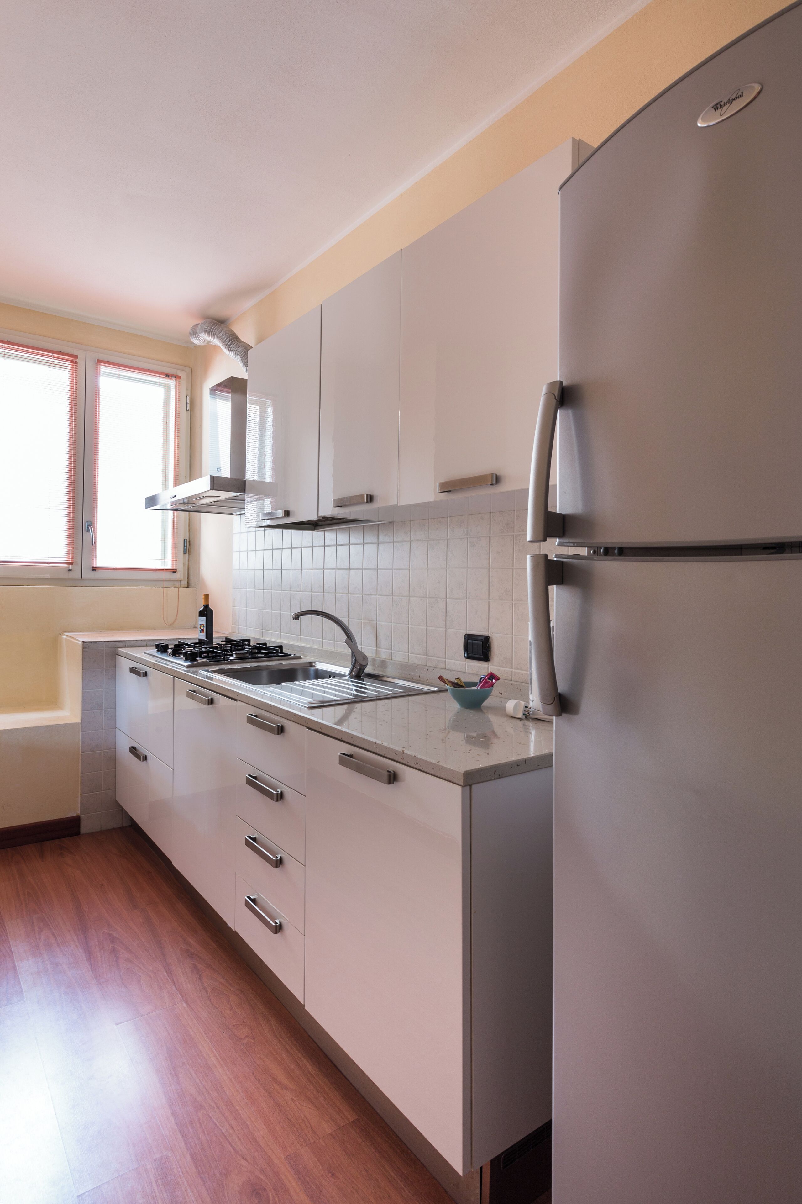 Une cuisine moderne dotée d’appareils électroménagers en acier inoxydable, de meubles blancs et d’une fenêtre avec des stores.