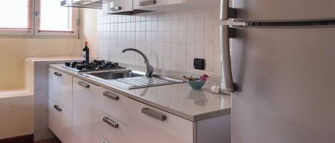 A modern kitchen with stainless steel appliances, white cabinets, and a window with blinds.