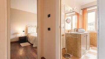 Quarto de hotel com cama, mesa de cabeceira, luminária e vista para a cidade pela janela.