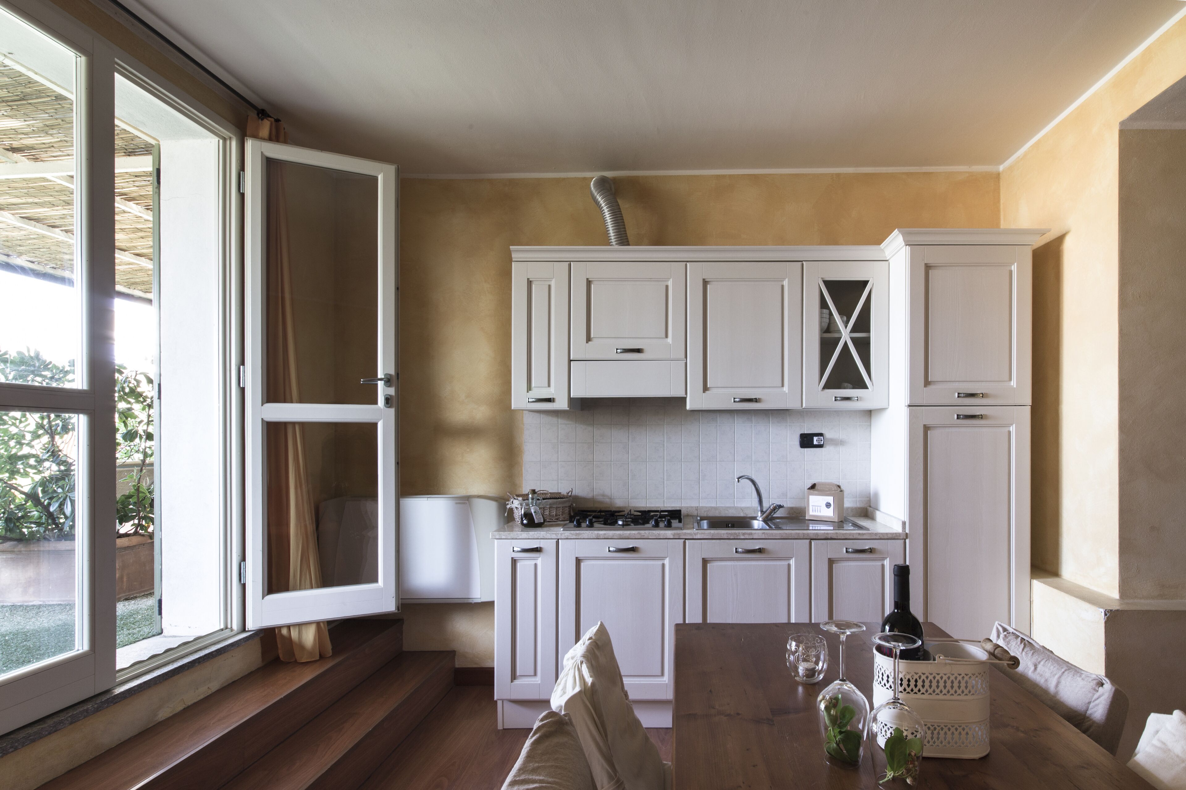 A kitchen with white cabinets, a wooden table, and a window with curtains.