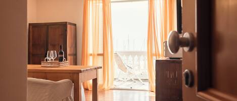 Una habitación con una mesa de madera, una silla y un armario. Tiene un balcón con barandilla blanca y cortinas naranjas.