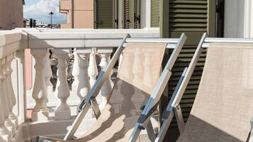A balcony with a white balustrade, a pair of beige canvas lounge chairs, and a view of adjacent buildings with green shutters.