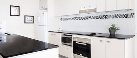 A modern kitchen with white cabinets, a black countertop, a microwave, an oven, and a small potted plant.