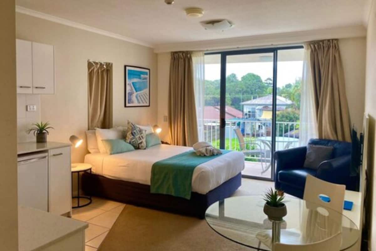 A modern hotel room with a bed, a desk, a chair, a balcony with a view, and a dining area.