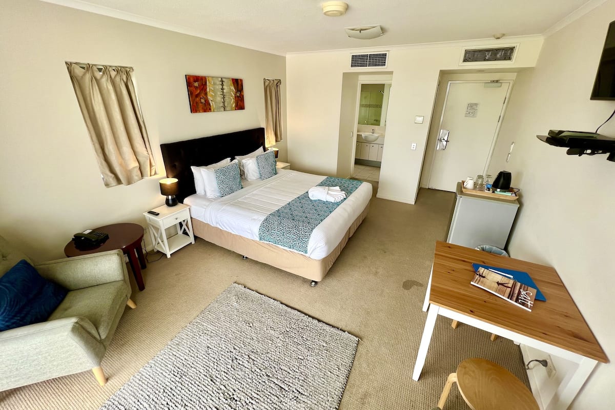 A hotel room with a bed, bedside table, lamp, chair, desk, and a view of the bathroom.