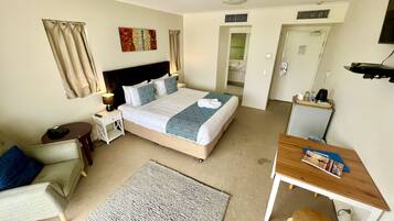 Ein Hotelzimmer mit Bett, Nachttisch, Lampe, Stuhl, Schreibtisch und Blick ins Bad.