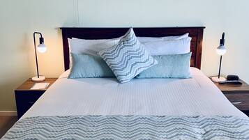 A neatly made bed with a patterned bedspread and pillows, flanked by bedside tables with lamps, in a room with a large landscape painting on the wall.