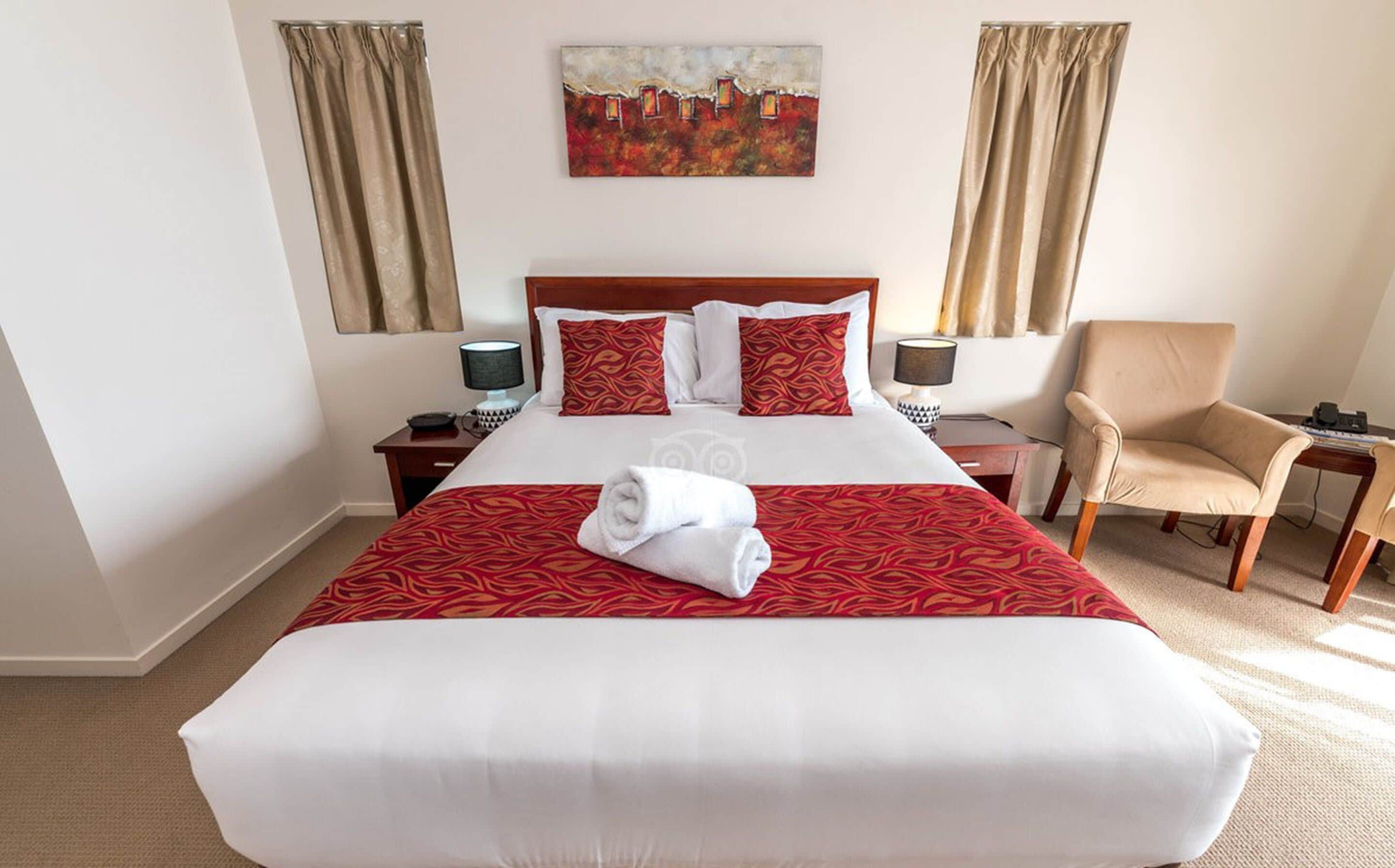 A hotel room with a large bed, two bedside tables, a chair, and a painting on the wall.