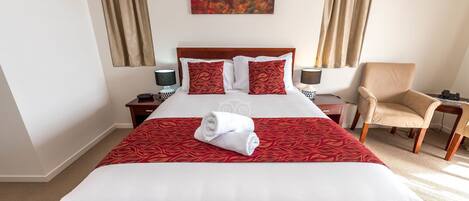 A hotel room with a large bed, two bedside tables, a chair, and a painting on the wall.