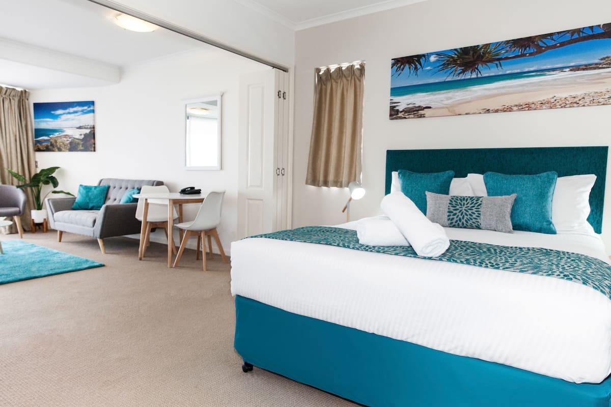 A hotel room with a bed, a desk, a chair, and a view of a beach.