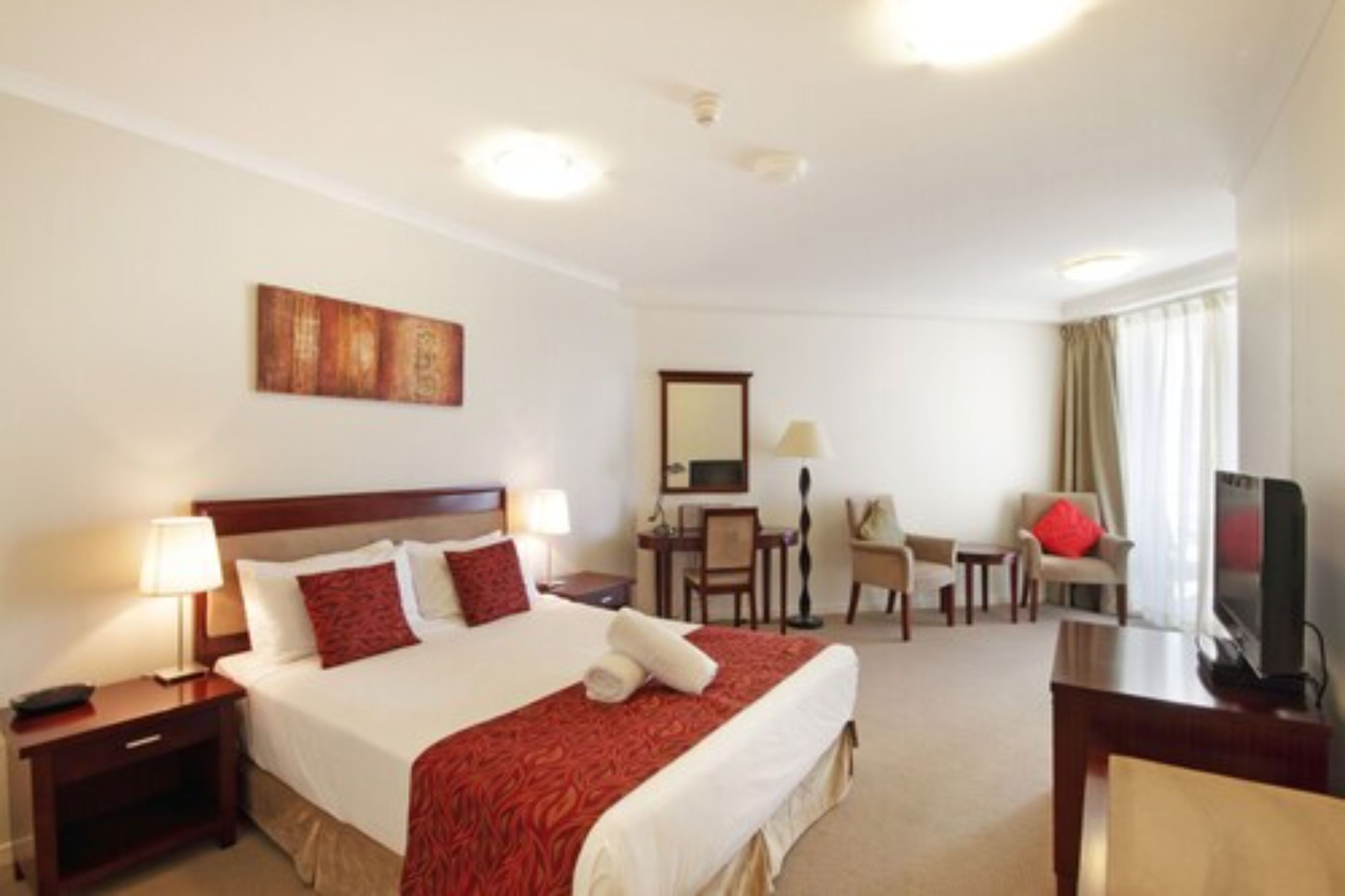 Una habitación de hotel con una cama grande, un escritorio, una silla, un televisor y una ventana con cortinas.