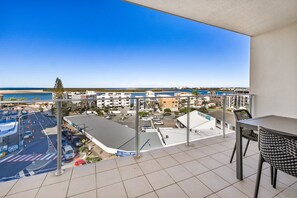 A balcony with a view of the beach and cityscape, including a parking lot and buildings. - Ocean Views Resort (Caloundra)