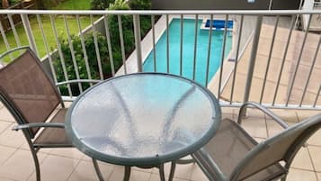 Un balcone con un tavolo in vetro e due sedie, con vista su una piscina.