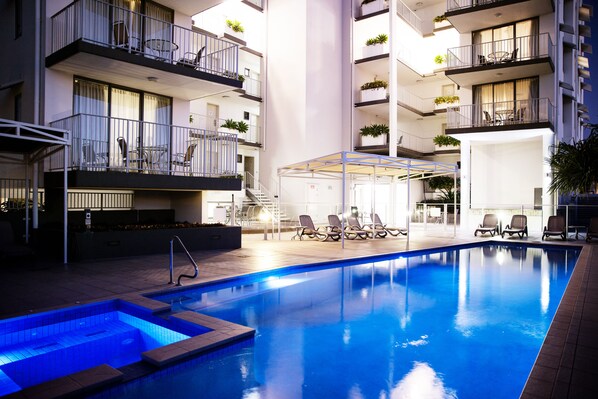 A swimming pool with lounge chairs, a covered seating area, and balconies with plants. - Ocean Views Resort (Caloundra)